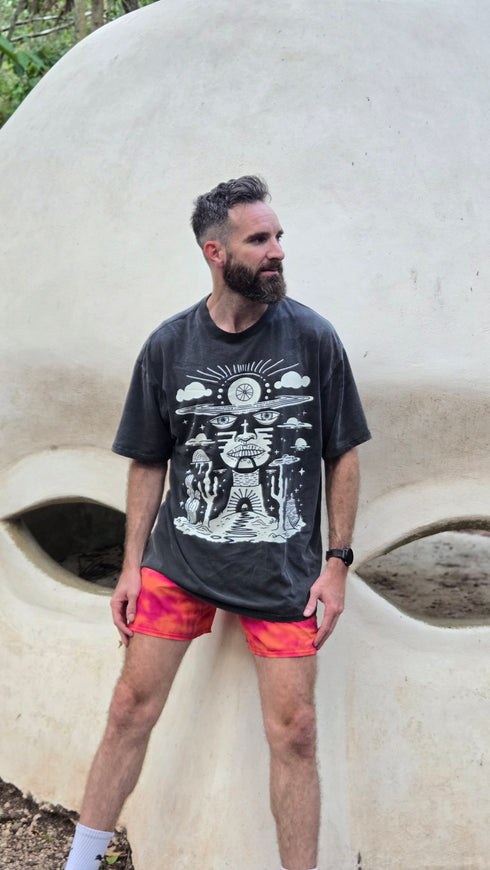 Man wearing a graphic t-shirt and red shorts standing in front of a large concrete structure.
